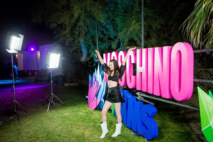 A girl posing for a photo next to a "Moschino" sign at the Moschino party in Indio, California