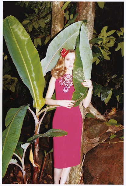 a model in a red dress hiding behind a large tropical plant