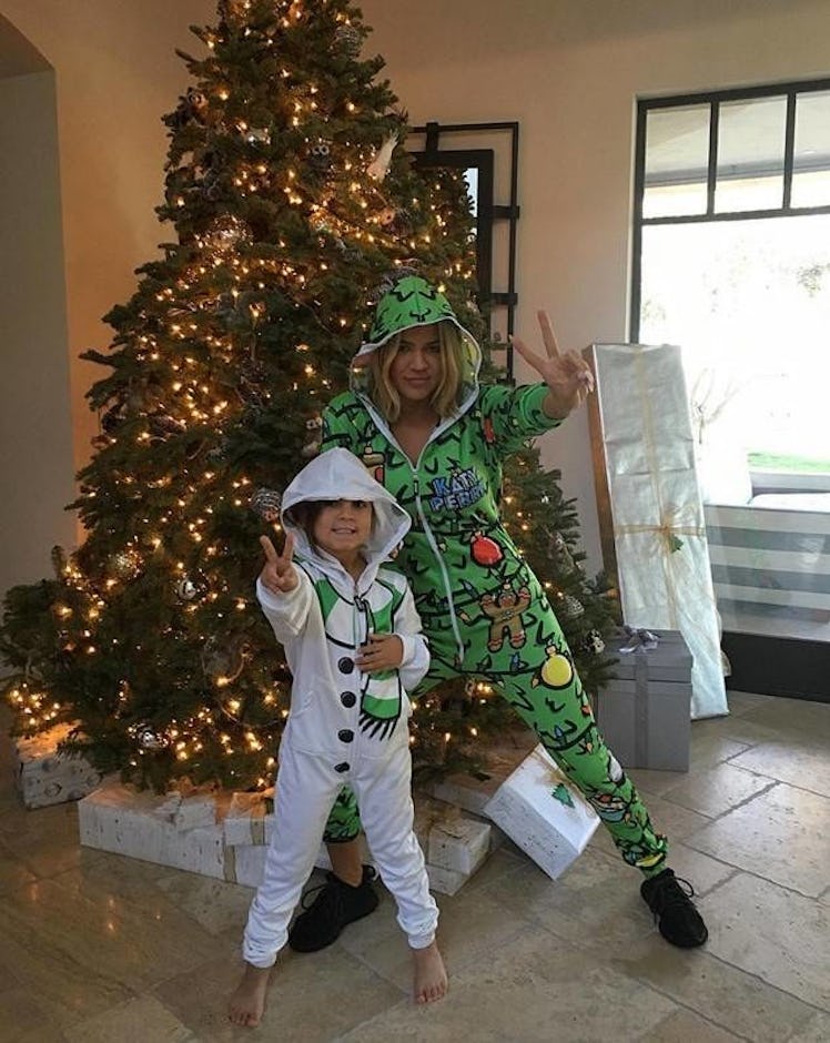 Khloe Kardashian and Mason Disick in green-white onesies posing next to a Christmas tree