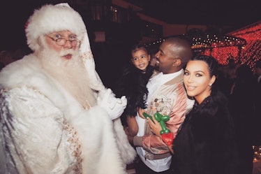 Kim Kardashian and Kanye West, who's holding North West posing next to a man in a Santa Claus costum...