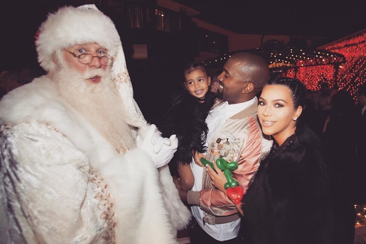 Kim Kardashian and Kanye West, who's holding North West posing next to a man in a Santa Claus costum...