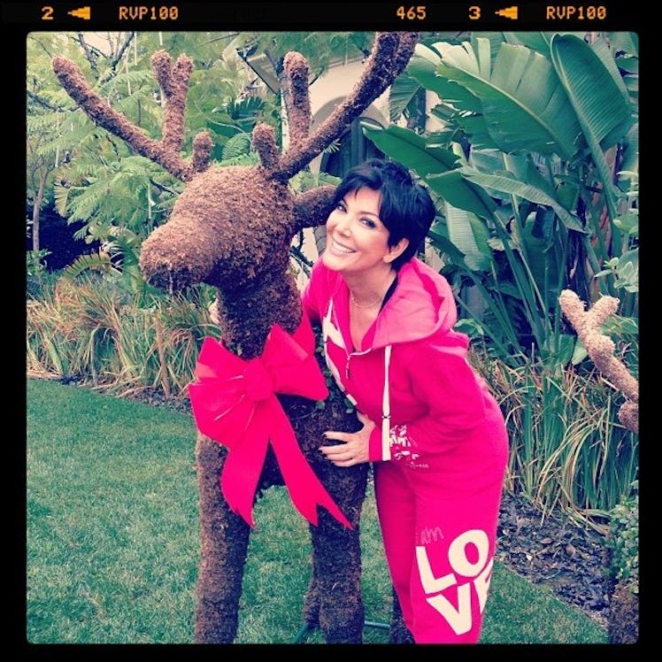 Kris Jenner smiling and posing in a red tracksuit next to a Christmas deer decoration statue in 2012