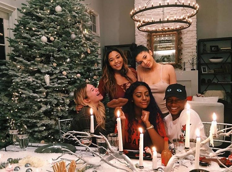 Kylie Jenner, Jordyn Woods, and three other friends sitting next to a Christmas decorated dinner tab...