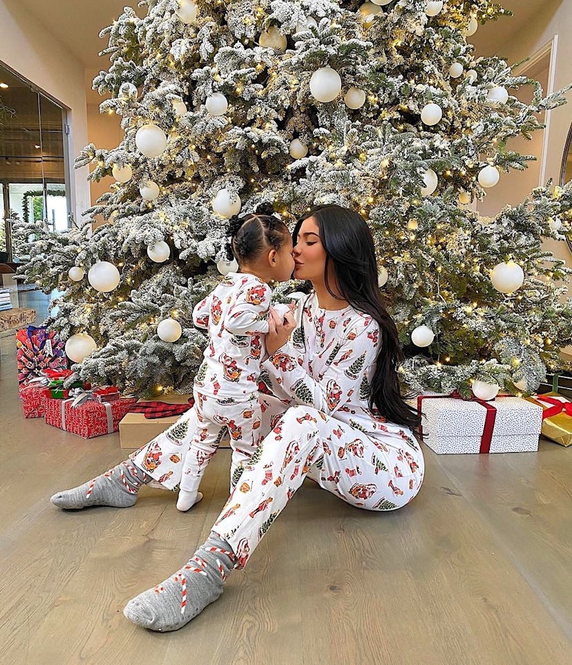 Kylie Jenner kissing Stormi Webster in matching white with print Christmas pyjamas underneath a Chri...
