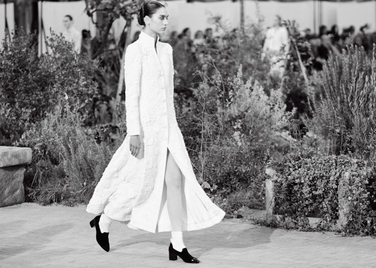 A model wearing a long white coat dress at the Chanel Couture Spring 2020 runway