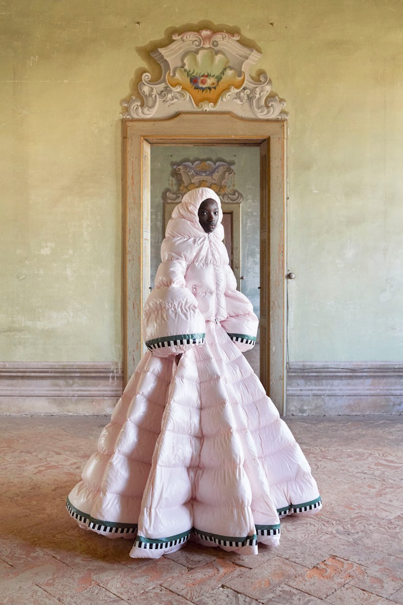 Model standing in an old living room, wearing a huge pink puffer dress with a hoodie on by Moncler P...