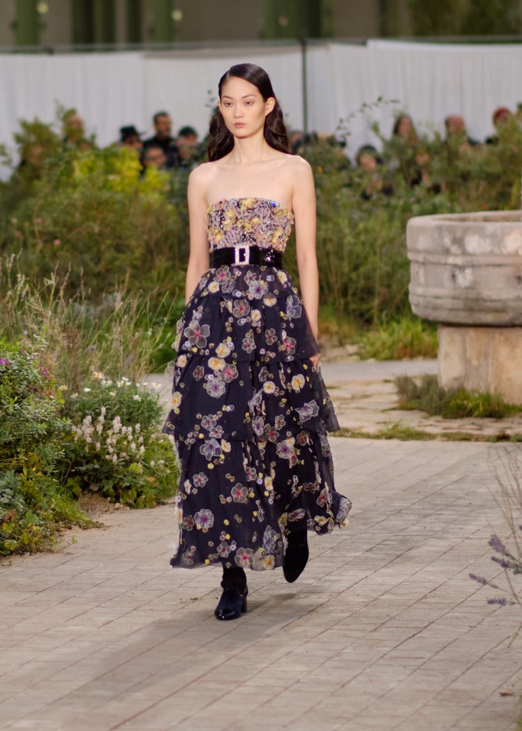 A model wearing a navy-vanilla floral dress with a black belt at the Chanel Couture Spring 2020 runw...