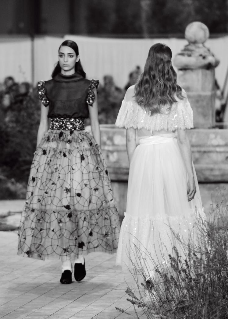 A model in a black top and black-white skirt and a model in a white dress at the Chanel Couture Spri...