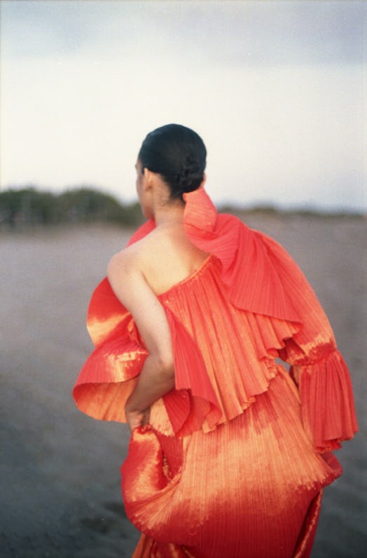 A model wearing an orange one-shoulder silk pleated dress by Capucci Roma.