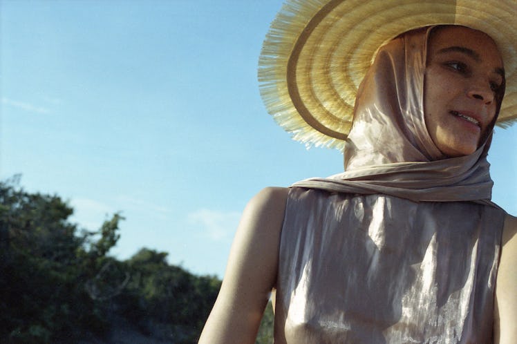 A model posing in a grey silk dress, a matching headscarf, and a straw hat by Capucci Roma.