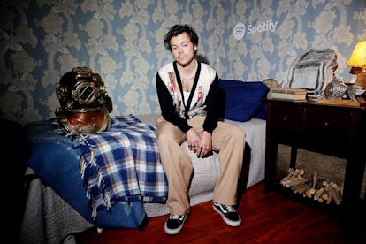 Harry Styles sitting on a bed wearing classical Old School Vans kicks paired with beige pants.