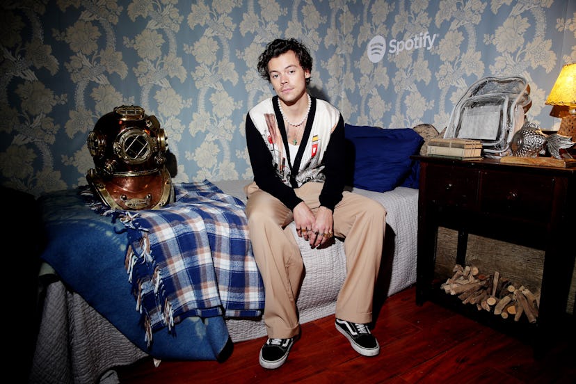 Harry Styles sitting on a bed wearing classical Old School Vans kicks paired with beige pants.