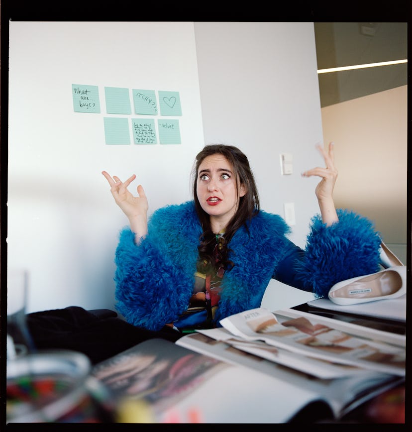 Catherine Cohen sitting and talking in a blue furry jacket and a black shirt