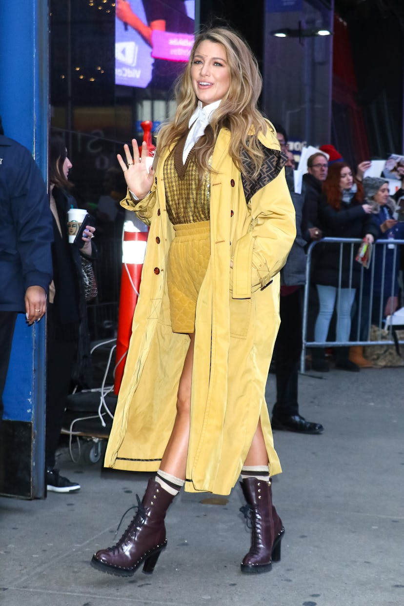 Blake Lively wearing mustard shorts, a pullover, and a Fendi trench coat while entering a building