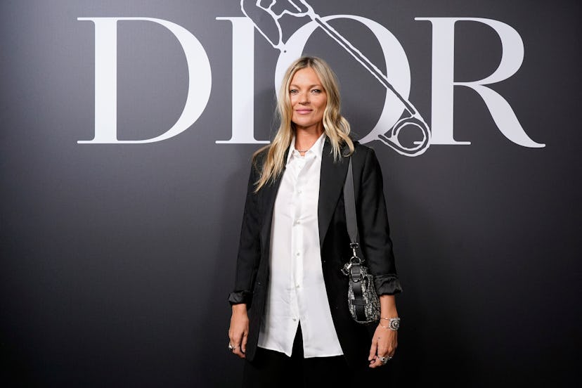 Kate Moss posing for the cameras at Dior's red carpet event in a white shirt, black suit and bag
