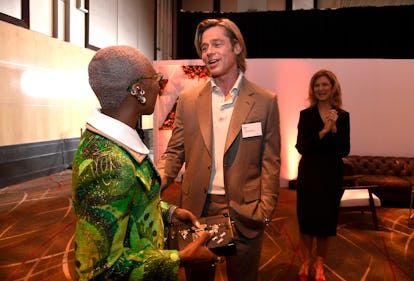 Brad Pitt at the Oscars Luncheon wearing a brown suit and a white shirt while speaking to a woman