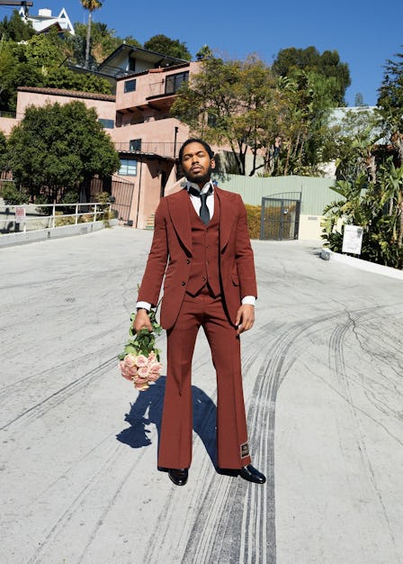 A man in a brown three-piece suit, holding a bouquet of roses 