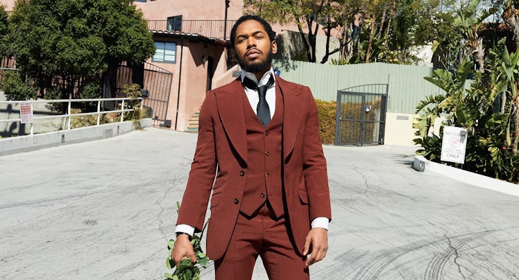 A man in a brown three-piece suit, holding a bouquet of roses