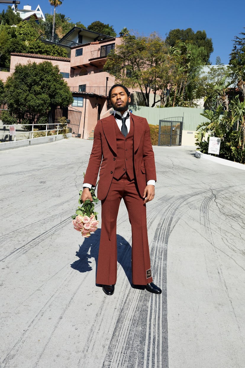 A man in a brown three-piece suit, holding a bouquet of roses