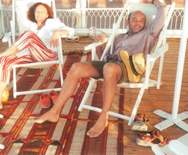 Diane von Furstenberg and Christian Louboutin sitting in white lounge chairs outside and smiling