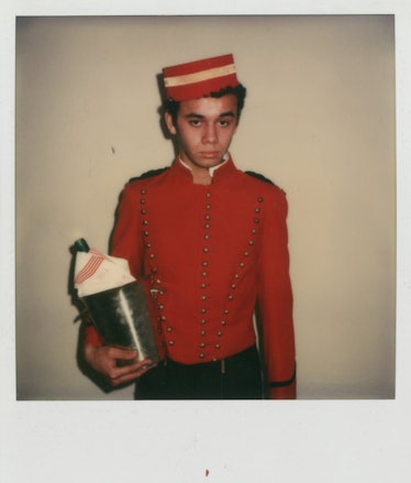 Young Christian Louboutin in a red hotel page uniform with a champagne holder