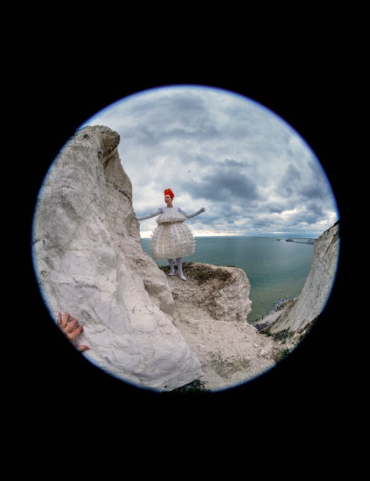 Sandy Powell standing on a sea cliff in a Noir Kei Ninomiya dress, Urstadt Swan gloves, Falke tights...
