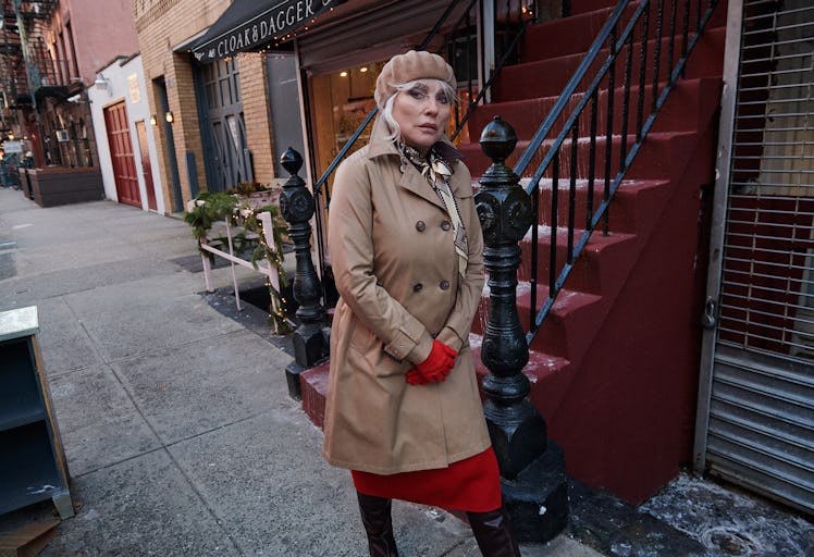 Debbie Harry in a Herno trench coat, a red Akris dress, a beige Clyde hat and red Paula Rowan gloves...