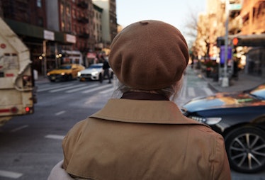 Debbie Harry looking at the street with her back turned in a beige Herno coat and a beige Clyde hat 