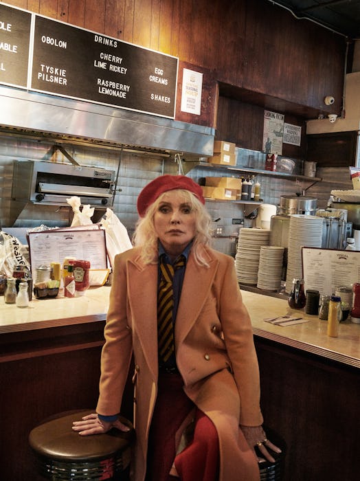 Debbie Harry in a restaurant in a Gucci coat, shirt, pants, tie, and belt, and a Lola Hats hat in be...