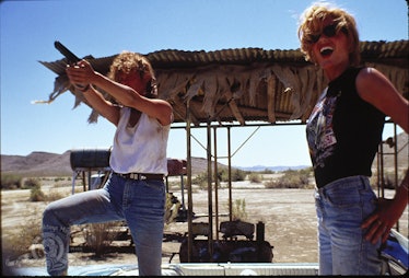 Susan Sarandon holding a gun and Geena Davis smiling next to her in a screenshot from a movie