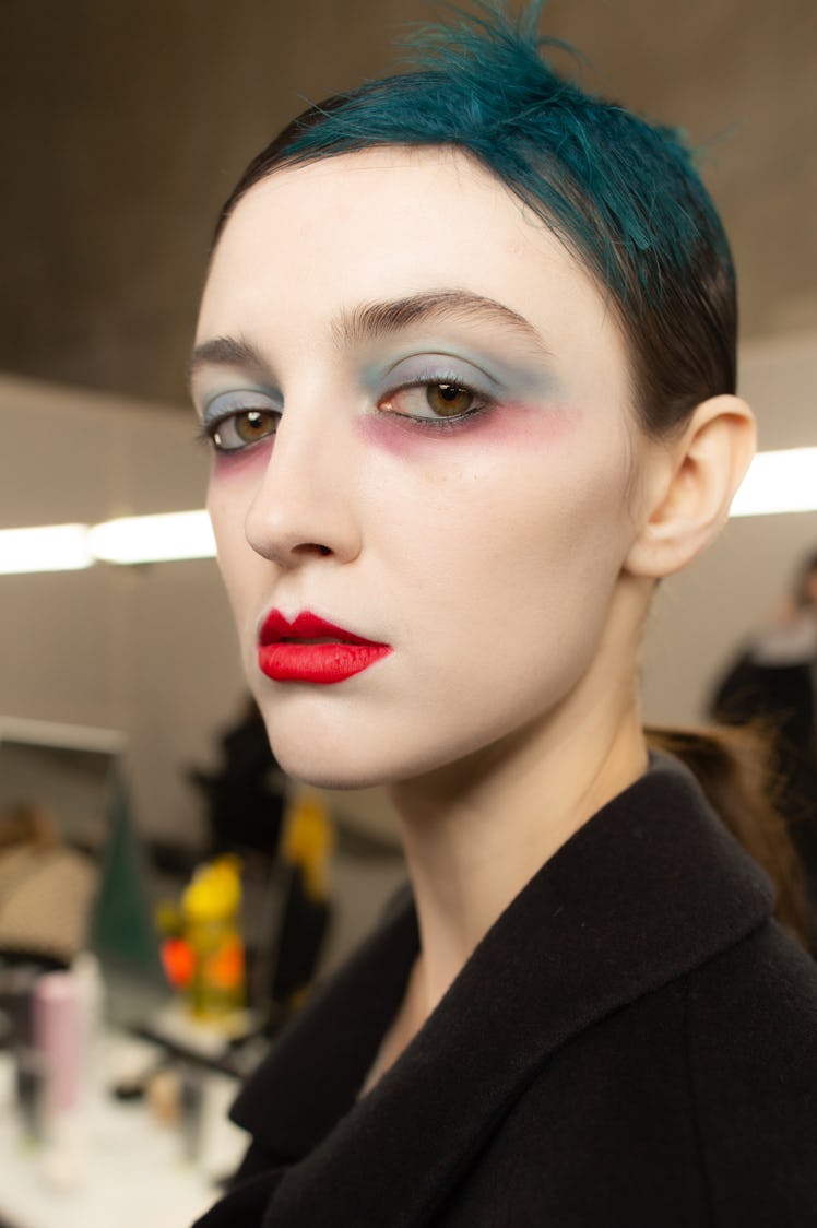 A female model posing with white makeup over her face, red lipstick, and green color in hair