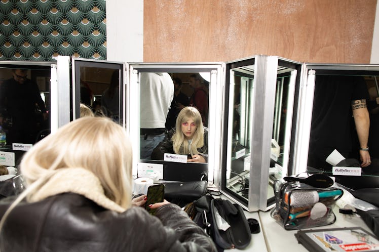 A model sitting next to a makeup station mirror backstage at the Matty Bovan fashion show