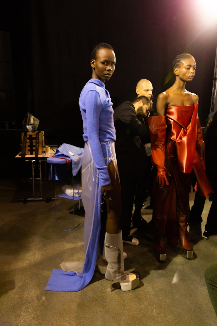 A model in a blue top and skirt and a model in a red dress backstage at the Rick Owens fashion show