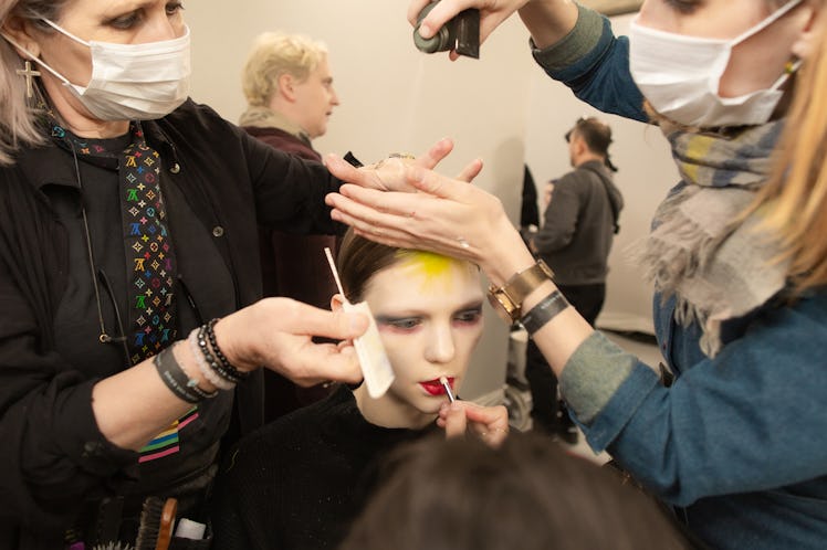 Makeup artist putting makeup on the face of a female model while two hairdressers are making her hai...