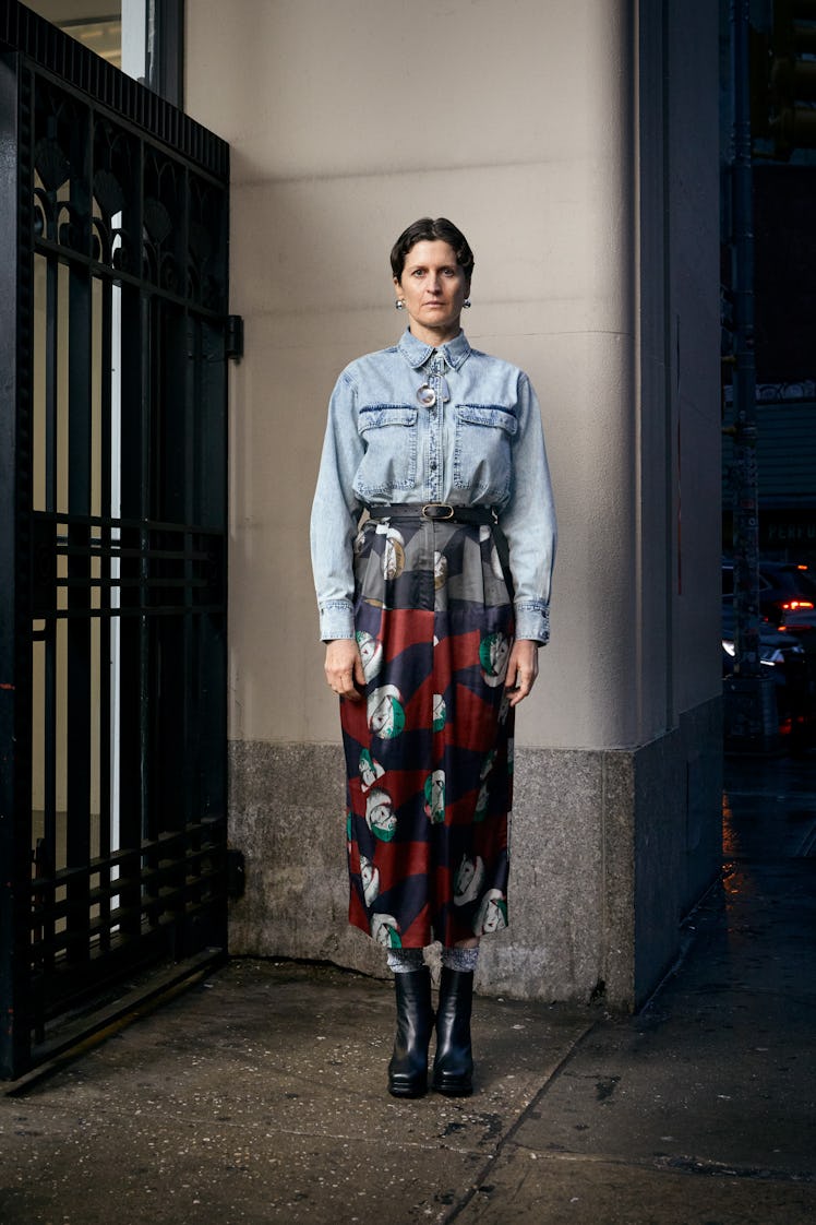 Alex Auder posing while wearing a denim shirt and skirt with a pattern at an entrance of a building