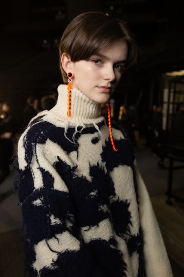 A model in a black-white sweater and orange earrings backstage at Off-White