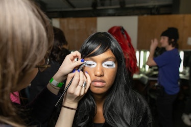 A model getting white eyeshadow applied by a makeup artist backstage at the Matty Bovan fashion show