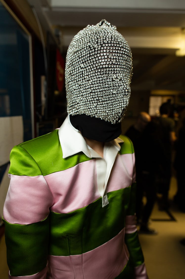 A model wearing a pink-green satin polo shirt and a diamond studded face mask at Richard Quinn‘s fal...