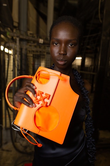 A model in a black dress holding an orange bag backstage at Off-White
