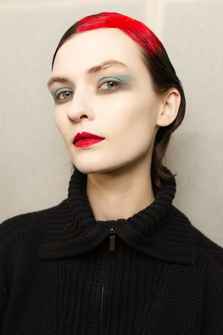 Closeup of a female model with white makeup all over her face and with a red and black hairstyle