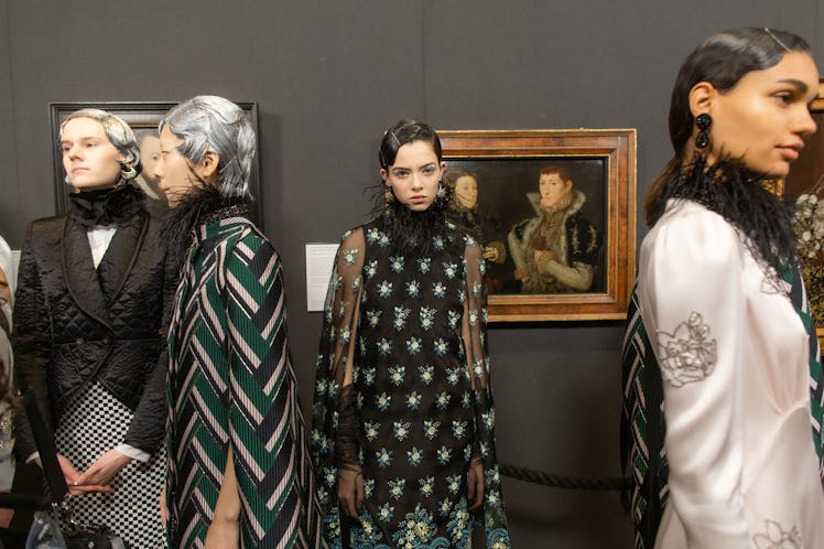 Models standing in an art gallery backstage, wearing pieces of designer Erdem Moralıoğlu 
