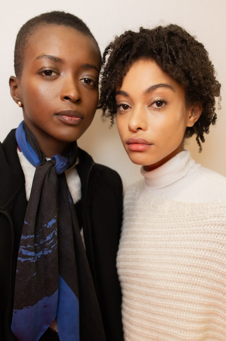 A model in a black coat and blue scarf and a model in a white sweater backstage at Balmain Fall 2020