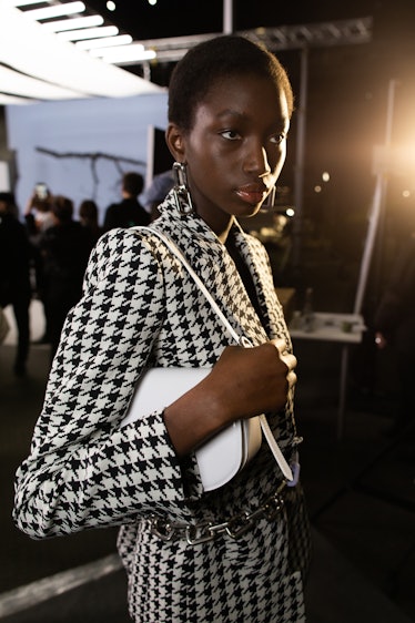 A model in a black-white tweed blazer holding a small white bag backstage at Off-White