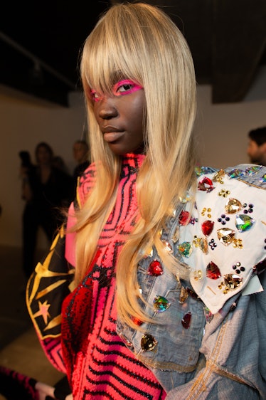 A model in a multi-colored, multi-patterned top with pink eyeshadow backstage at the Matty Bovan fas...