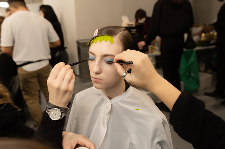 Two makeup artists putting blue eye makeup on the face of a female model