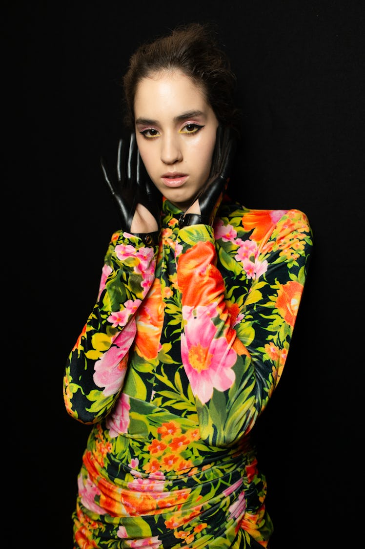 A model in a green-pink floral dress and black leather gloves backstage at Richard Quinn‘s fall coll...