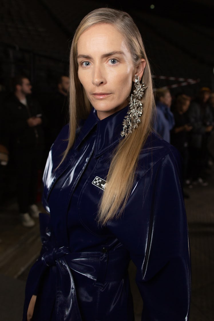 A model in a black latex coat and studded earrings backstage at Off-White