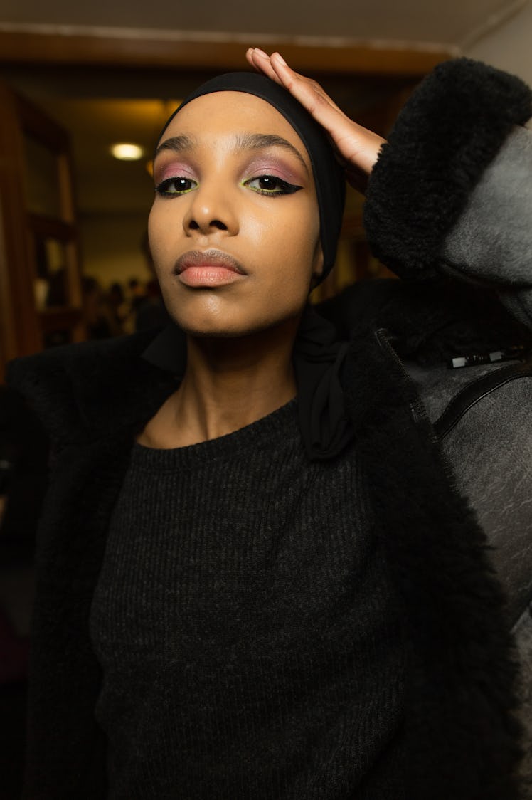 A close-up portrait of a model in a black jacket backstage at Richard Quinn‘s fall collection 