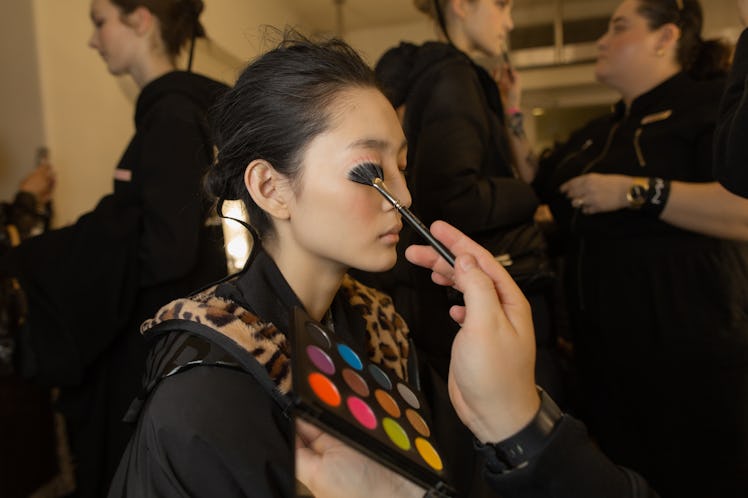 A model sitting with close eyes and a makeup artist applying makeup on her face at Richard Quinn‘s f...