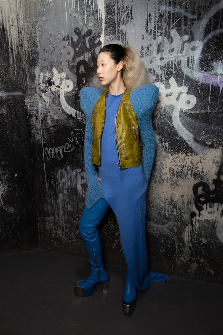 A model in a blue jumpsuit and olive waistcoat backstage at the Rick Owens fashion show